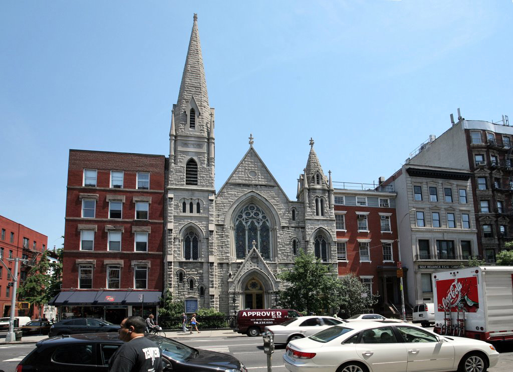 Horizontal color photo of Renaissance Revival-style church with two towers, one larger than the other, and other buildings on Second Avenue